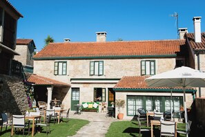 A stone building with a tiled roof, outdoor seating area with tables and chairs, and a pathway leading to the entrance. - CASA DE COSTOIA (Ames)