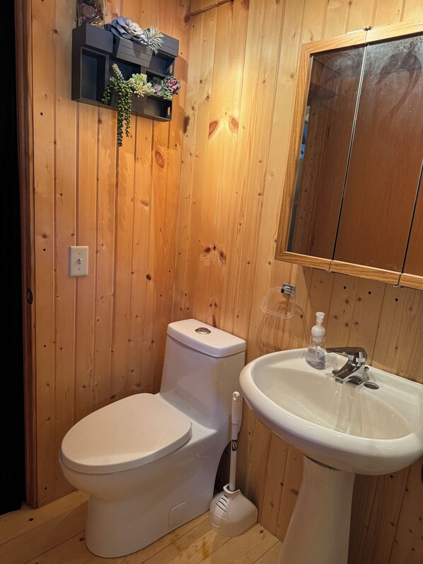 A wooden-paneled bathroom with a toilet, sink, and a shelf with plants. - Log cabin with WiFi in quiet community above Custer. (Custer)