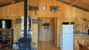 A wooden cabin interior with a fireplace, a television, a kitchen area, and a clock on the wall. - Log cabin with WiFi in quiet community above Custer.  (Custer)