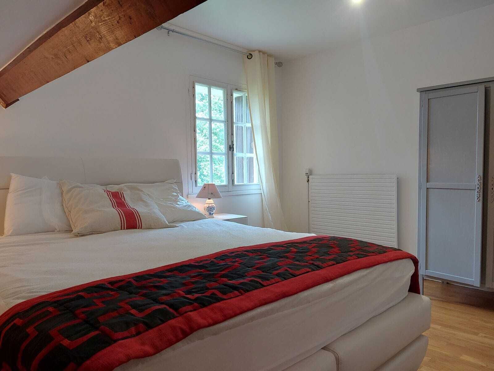 A bedroom with a bed, a window with curtains, a radiator, and a wardrobe.
