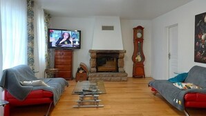 A living room with two red sofas, a glass coffee table, a fireplace, a large clock, and a television on the wall. - Beautiful country house located in Eure-et-Loire in an idyllic setting (La Bazoche Gouet)