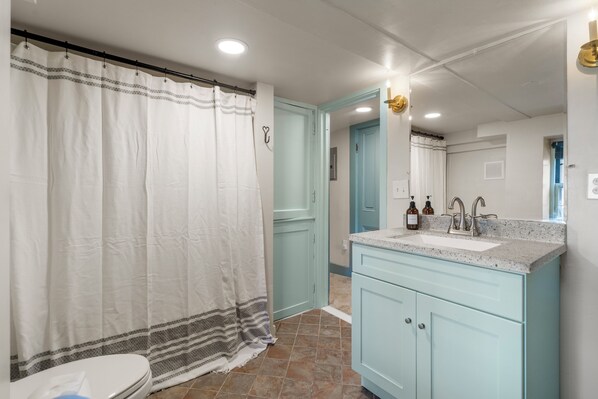 Un baño con cortina de ducha blanca, un lavabo con encimera y armarios azul claro.