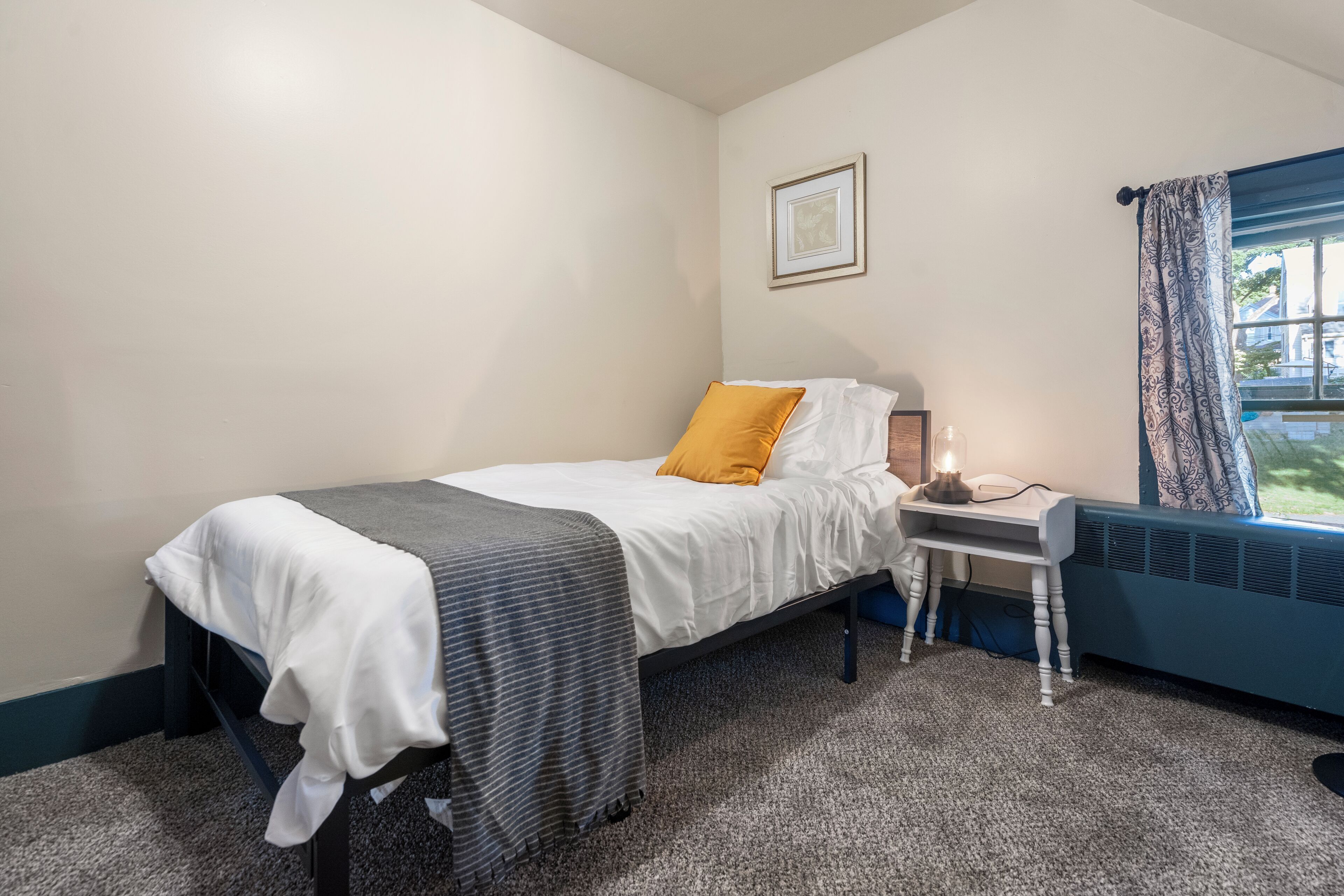 A neatly arranged bedroom with a bed, bedside table, and a window with curtains.