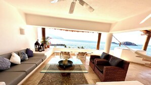 A modern living room with a sofa, a wicker chair, a glass coffee table, and a view of the sea. - Spacious villa in Ixtapa with beautiful ocean views (Ixtapa Zihuatanejo)