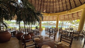 A restaurant with wooden tables and chairs, thatched roof, and potted plants. - Spacious villa in Ixtapa with beautiful ocean views (Ixtapa Zihuatanejo)