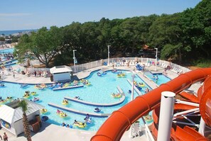 A water park with multiple pools, a large water slide, and a fenced area with lounge chairs. - MH22b | Ocean View 4BR w/ Huge Deck | Steps to Sand! Comp Golf Cart (Myrtle Beach)