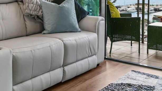 Ein modernes Wohnzimmer mit grauem Sofa, einem gemusterten Teppich und Blick auf eine Marina durch große Fenster.