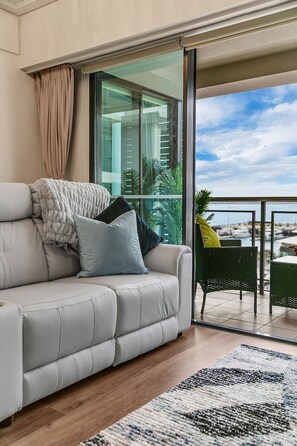 A modern living room with a grey sofa, a patterned rug, and a view of a marina through large windows. - Viaduct Victory Sub Penthouse (Auckland)