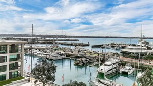 Ein Yachthafen mit mehreren anglegerten Booten, ein modernes Gebäude mit großen Fenstern und freier Sicht auf das Wasser und den fernen Stadtpanoramahimmel.