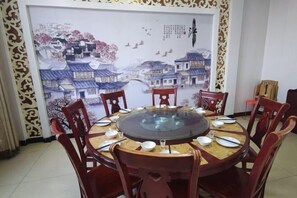 Une table de salle à manger ronde, entourée de huit chaises en bois, mise pour un repas avec des assiettes, des bols et des baguettes.