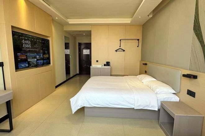 A hotel room with a large bed, a bedside table, a mirror, and a wall-mounted TV.