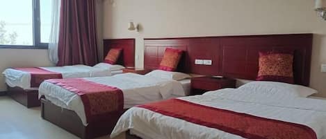 Habitación de hotel con tres camas, cada una con colcha roja y blanca, y un ventanal grande con cortinas.