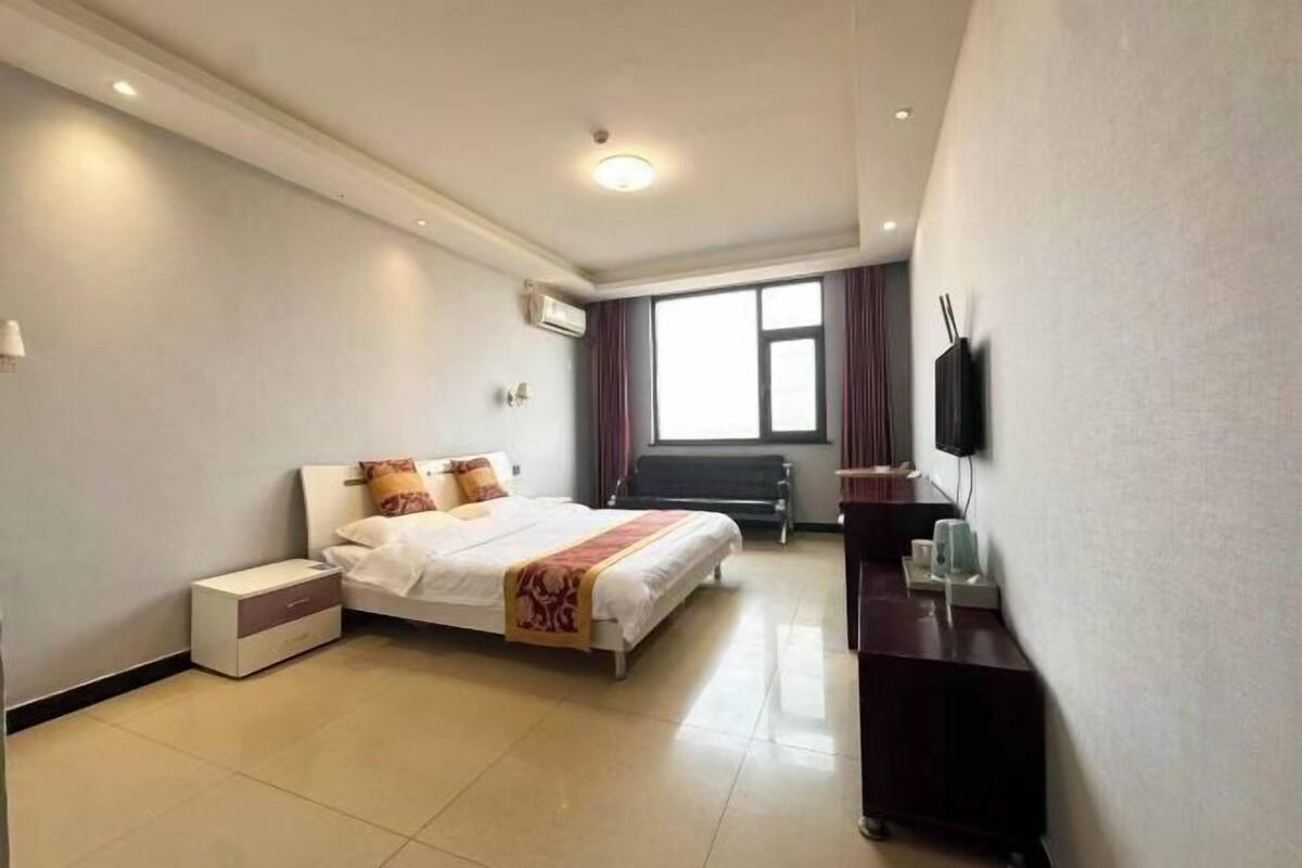 Habitación de hotel con cama, mesita de noche, televisor y ventana con cortinas.