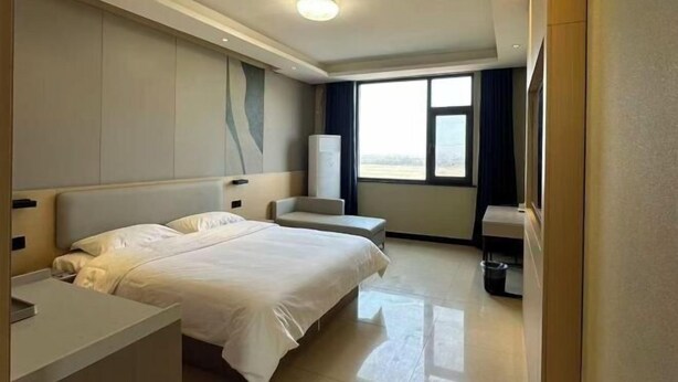 Una habitación de hotel con una cama grande, una mesita de noche, una silla, una ventana y un cubo de basura.
