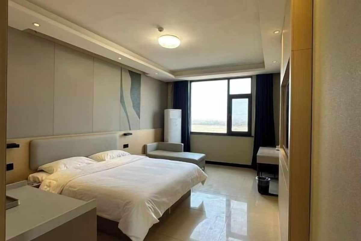 Una habitación de hotel con una cama grande, una mesita de noche, una silla, una ventana y un cubo de basura.