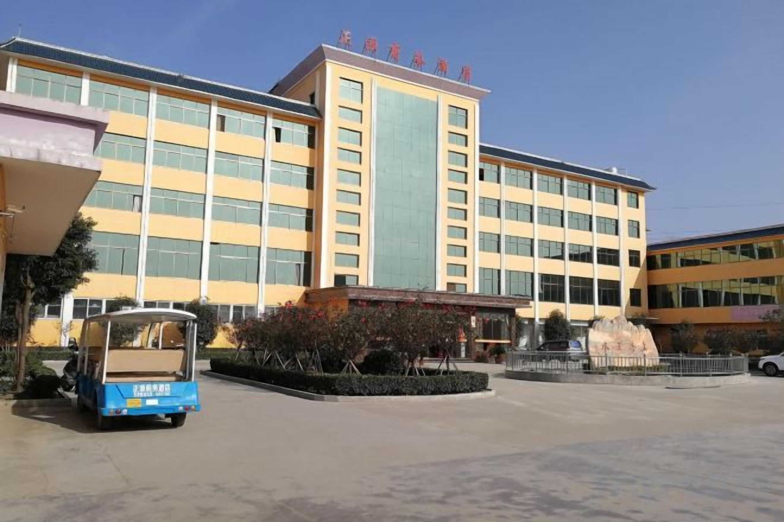 A multi-story building with a central entrance, a blue vehicle in the foreground, and a clear sky.
