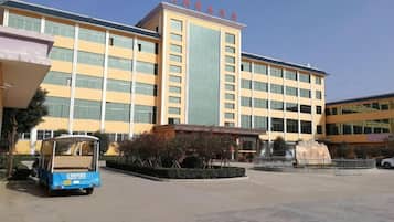 A multi-story building with a central entrance, a blue vehicle in the foreground, and a clear sky.