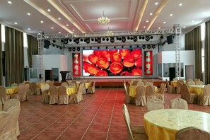 Un salón de banquetes con un escenario, filas de mesas y sillas.