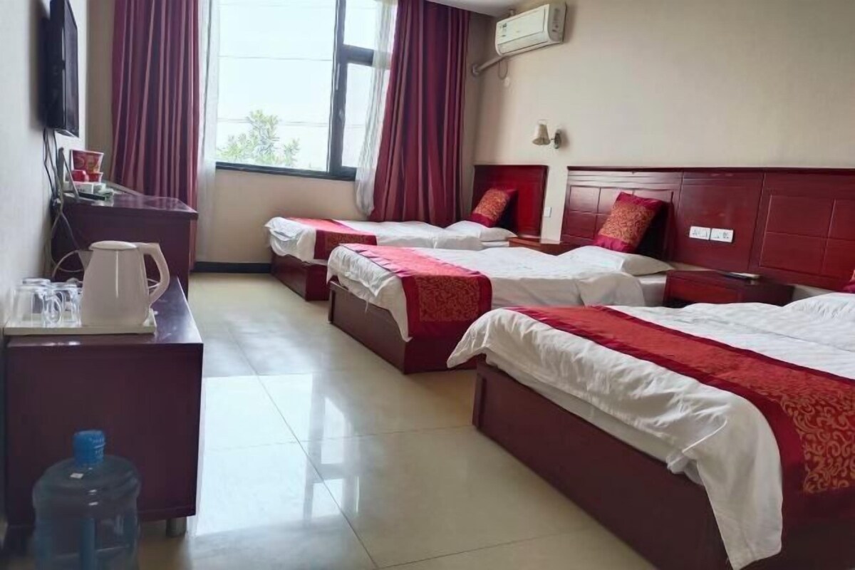 Une chambre d’hôtel avec trois lits, un bureau avec une bouilloire et un grand distributeur d’eau.