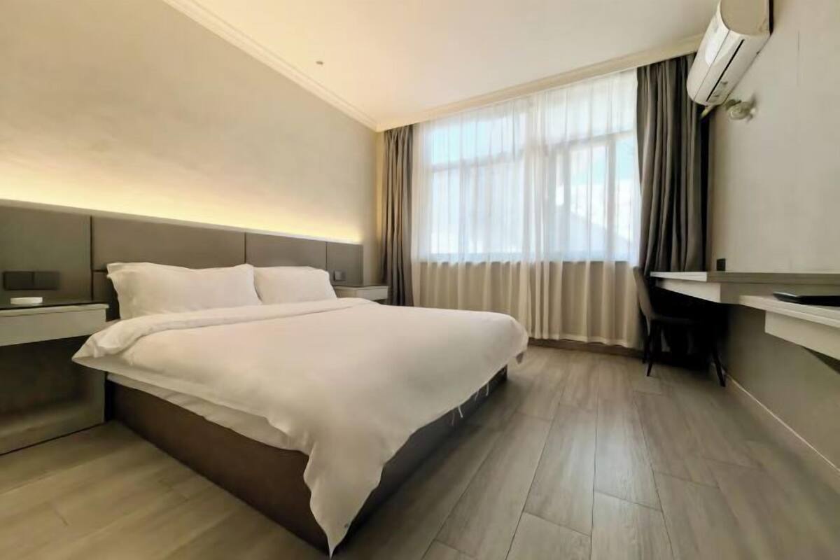 Ein modernes Hotelzimmer mit einem großen Bett, Nachttischen, einem Schreibtisch und einem fenster mit Vorhängen.