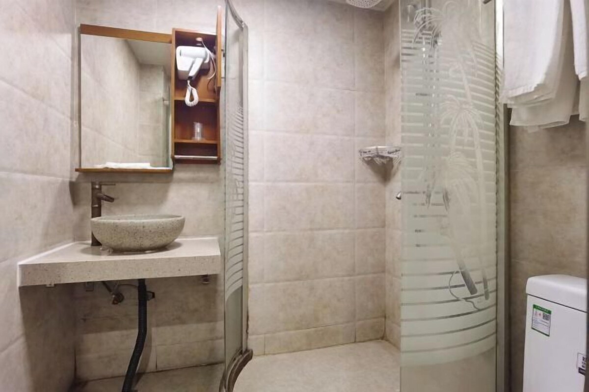 A bathroom with a large mirror, a bowl sink, a glass shower enclosure, and a white toilet.