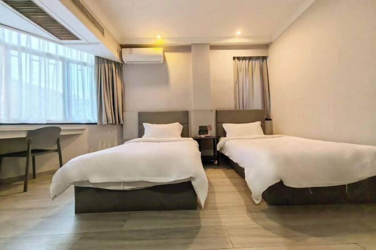 Ein Hotelzimmer mit zwei Betten, einem Schreibtisch, einem Stuhl und einem Fenster mit Vorhängen.
