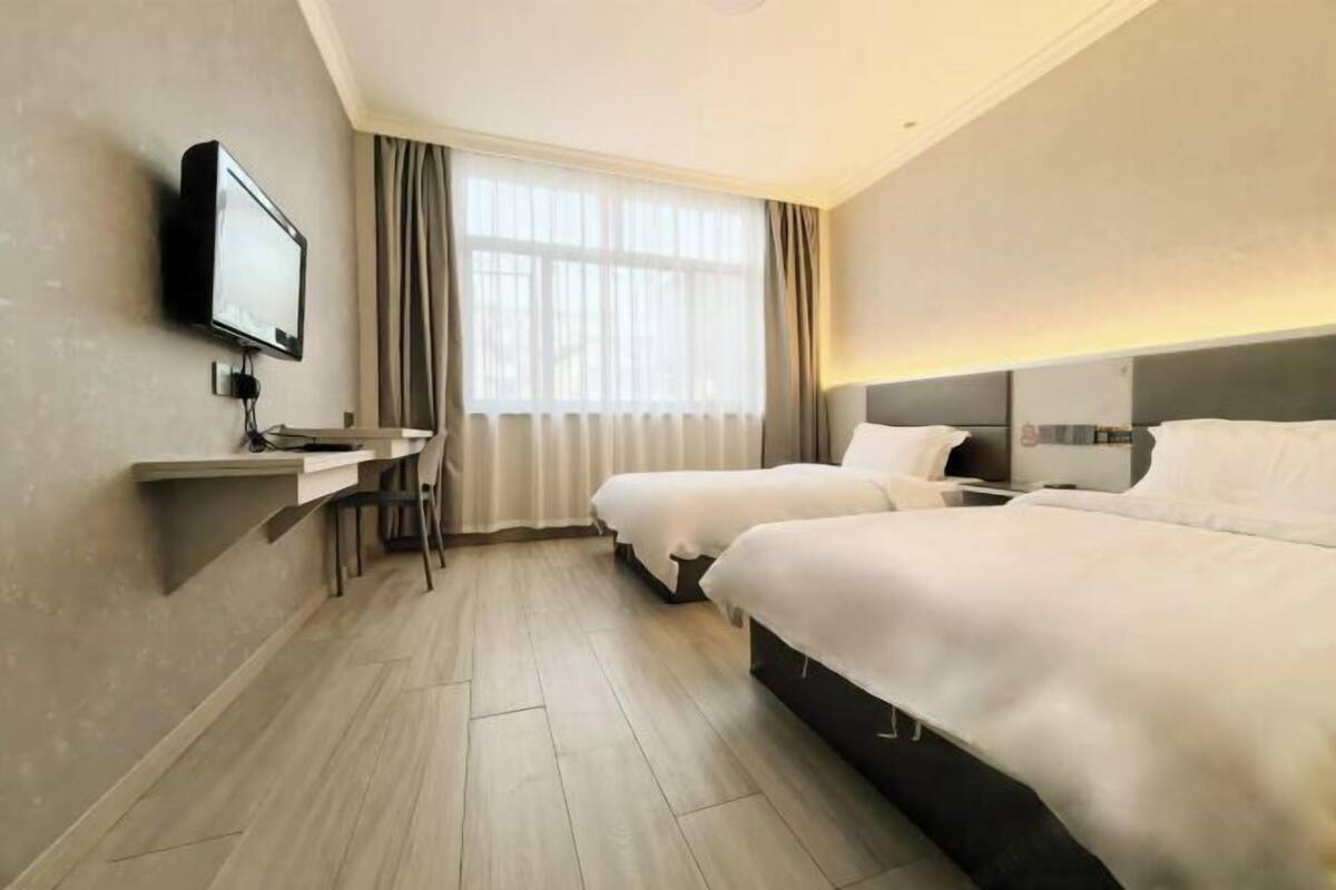 Ein Hotelzimmer mit zwei Betten, einem Fernseher, einem Schreibtisch und einem Fenster mit Vorhängen.