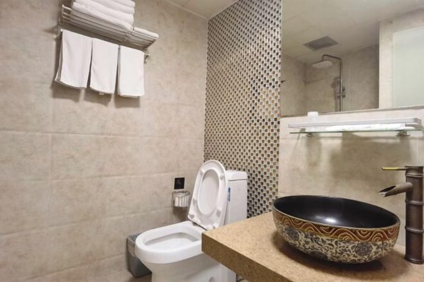 A bathroom with a toilet, a sink with a decorative bowl, and a towel rack with folded towels. - Jingjiang Hotel (Linhai)