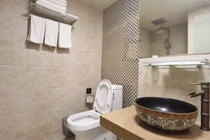 Un baño con inodoro, un lavabo con un cuenco decorativo y un perchero con toallas dobladas.