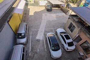 Ein Parkplatz mit mehreren parkenden Autos, ein Gebäude mit gelber Fassade und eine kleine Struktur im Hintergrund.