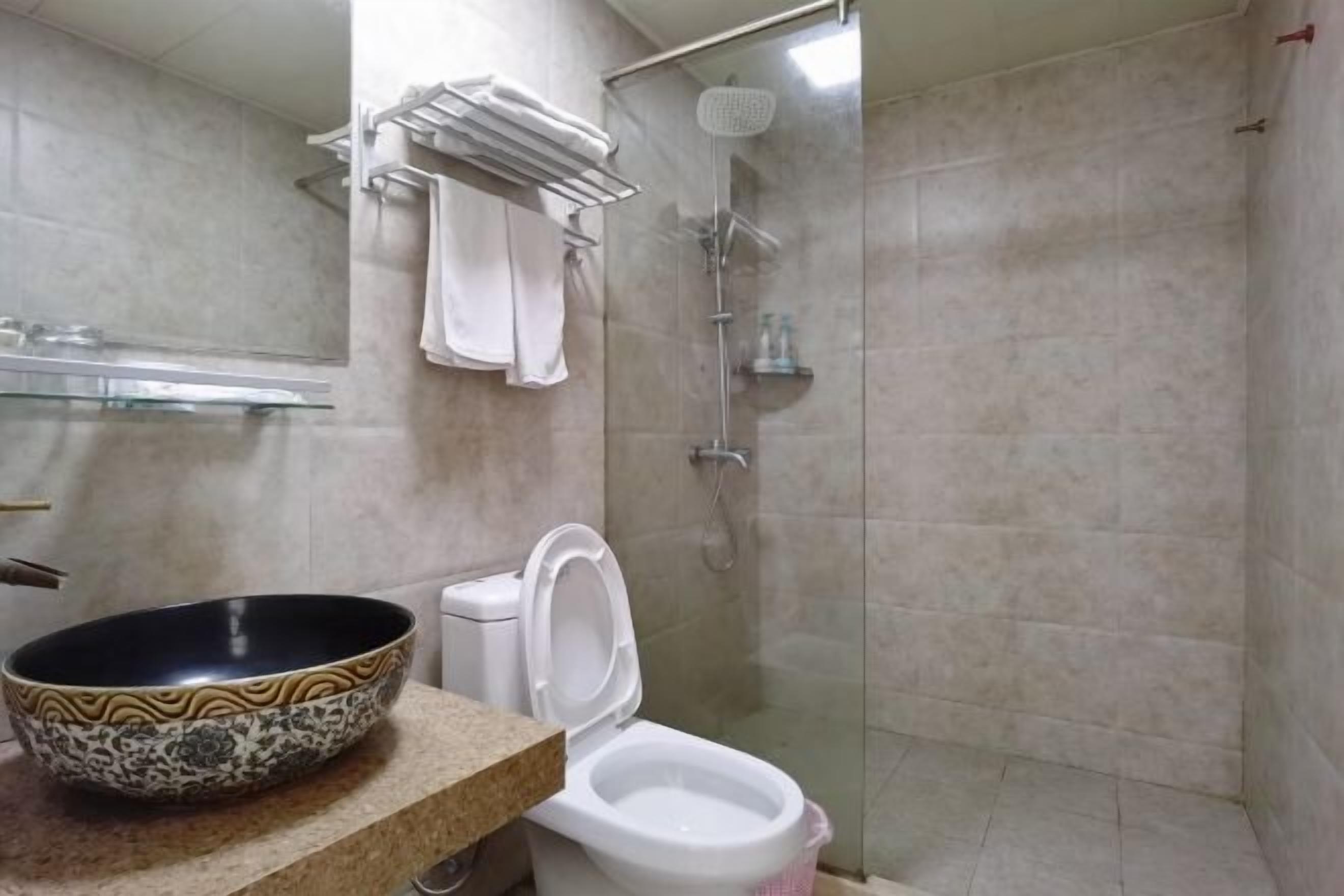 A bathroom with a toilet, a glass shower enclosure, and a decorative bowl on the counter.
