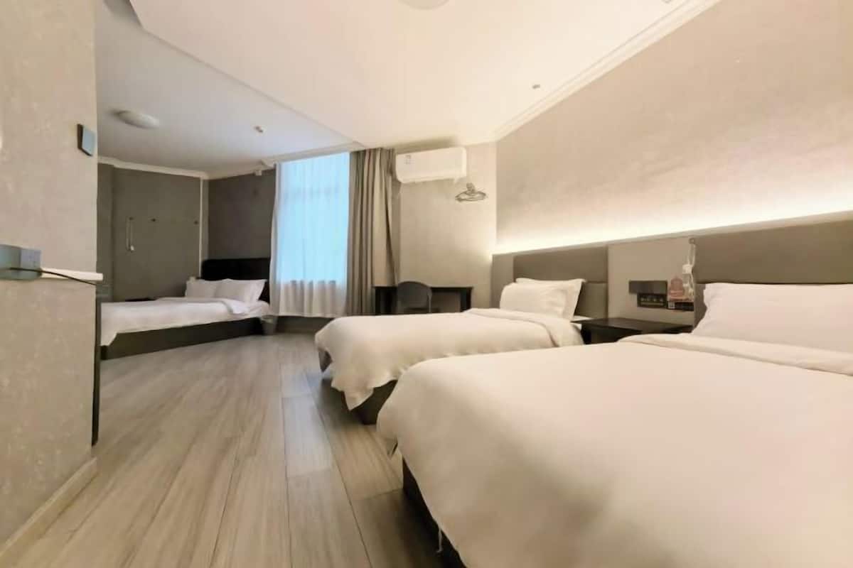 Ein Hotelzimmer mit zwei Betten, einem Schreibtisch, einem Sessel, einem Fenster mit Vorhängen und einer Klimaanlage.