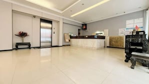 A hotel reception area with a marble reception desk, a reception counter, a digital screen, and a wall-mounted information board. - Jingjiang Hotel (Linhai)