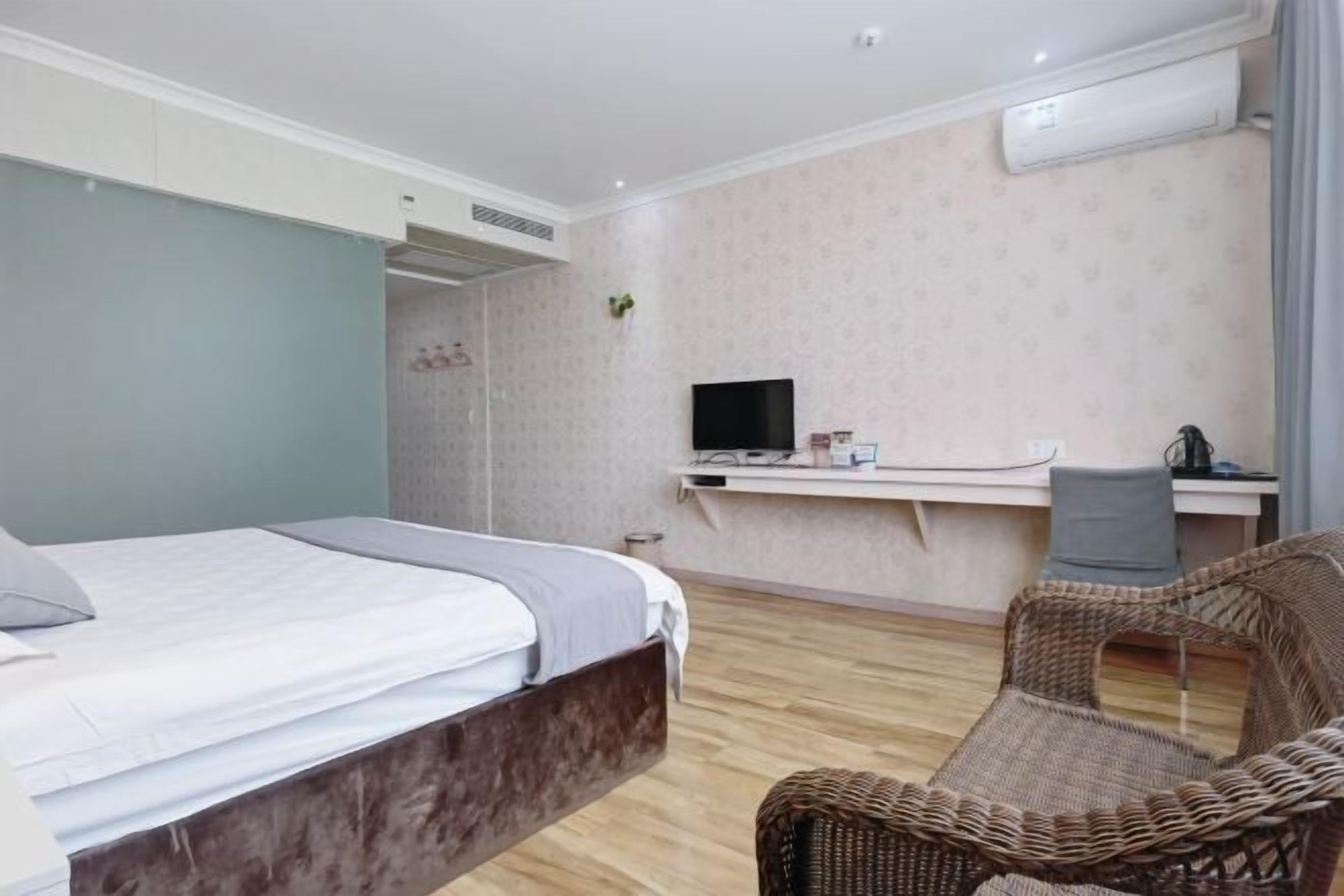 Ein Schlafzimmer mit einem Bett, einem Schreibtisch mit Computer, einem Stuhl und einer Klimaanlage.