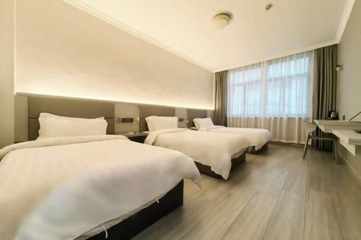 Ein Hotelzimmer mit drei Betten, einem Schreibtisch und einem großen Fenster mit Vorhängen.
