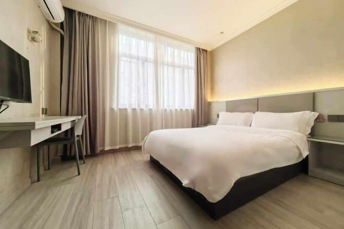 Ein Hotelzimmer mit einem Bett, einem Schreibtisch, einem Sessel, einem Fernseher und einem Vorhangfenster.