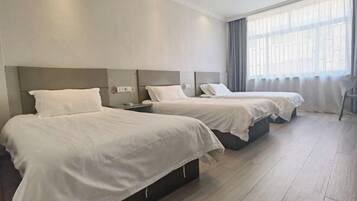 A hotel room with two beds, a nightstand, and a large window with curtains.