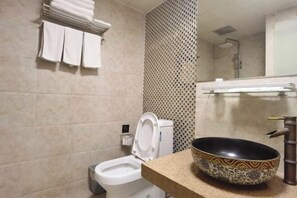 A bathroom with a toilet, sink, and a decorative bowl on the counter. - Jingjiang Hotel (Linhai)