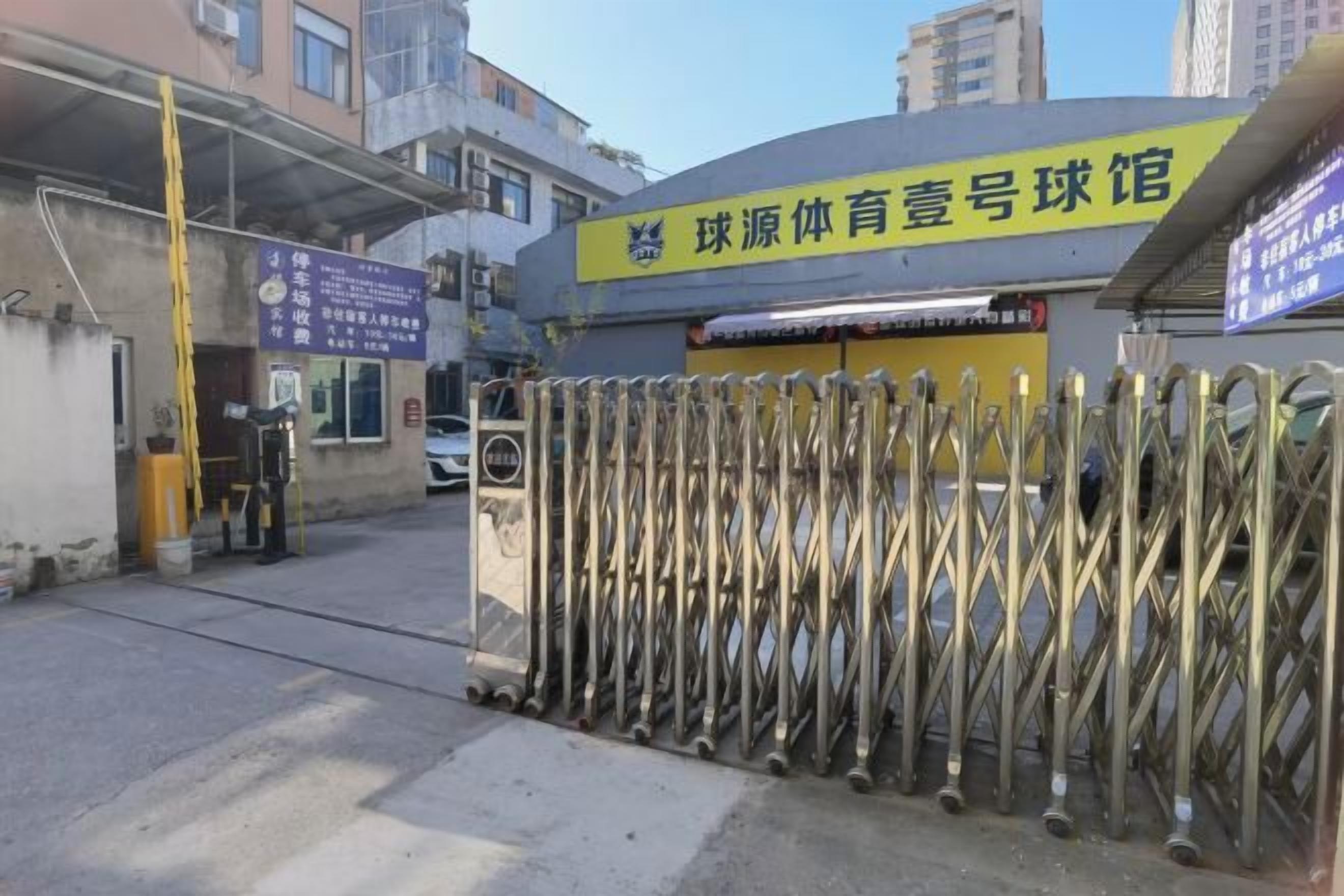 A sports facility entrance with a metal gate and a yellow sign.
