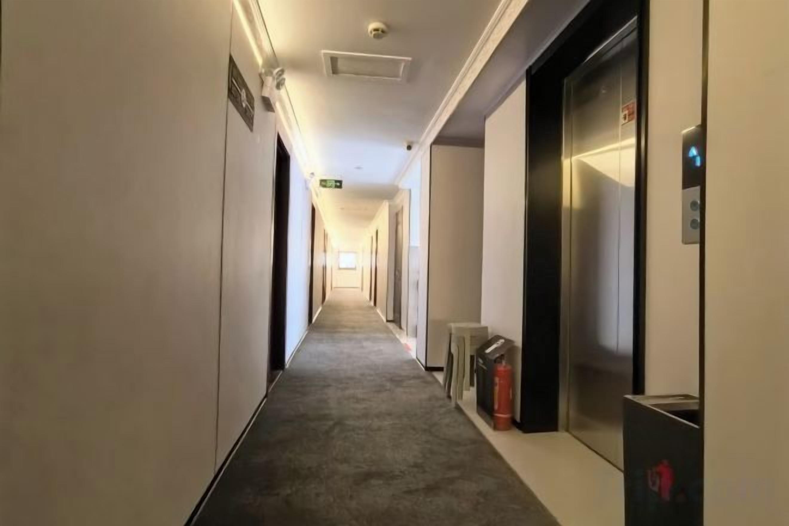 A hotel corridor with an elevator, fire extinguisher, and emergency exit sign.