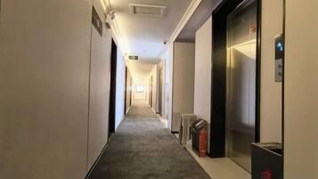 A hotel corridor with an elevator, fire extinguisher, and emergency exit sign.