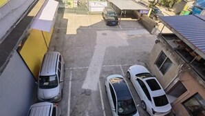 A parking area with several cars, a yellow wall, and a building with a metal roof. - Jingjiang Hotel (Linhai)
