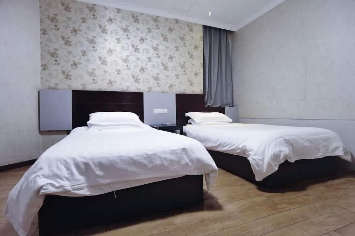 Ein Hotelzimmer mit zwei Einzelbetten, Holzboden und einem Blumenmuster an der Tapete.