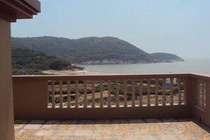 A balcony with a view of a beach and mountains. - Caiyuan Bihai Yuntian Hotel (Shengsi)