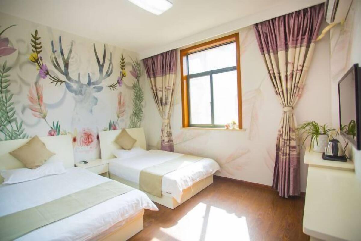 A room with two beds, a window, curtains, a TV, and a wall with a deer and floral mural.