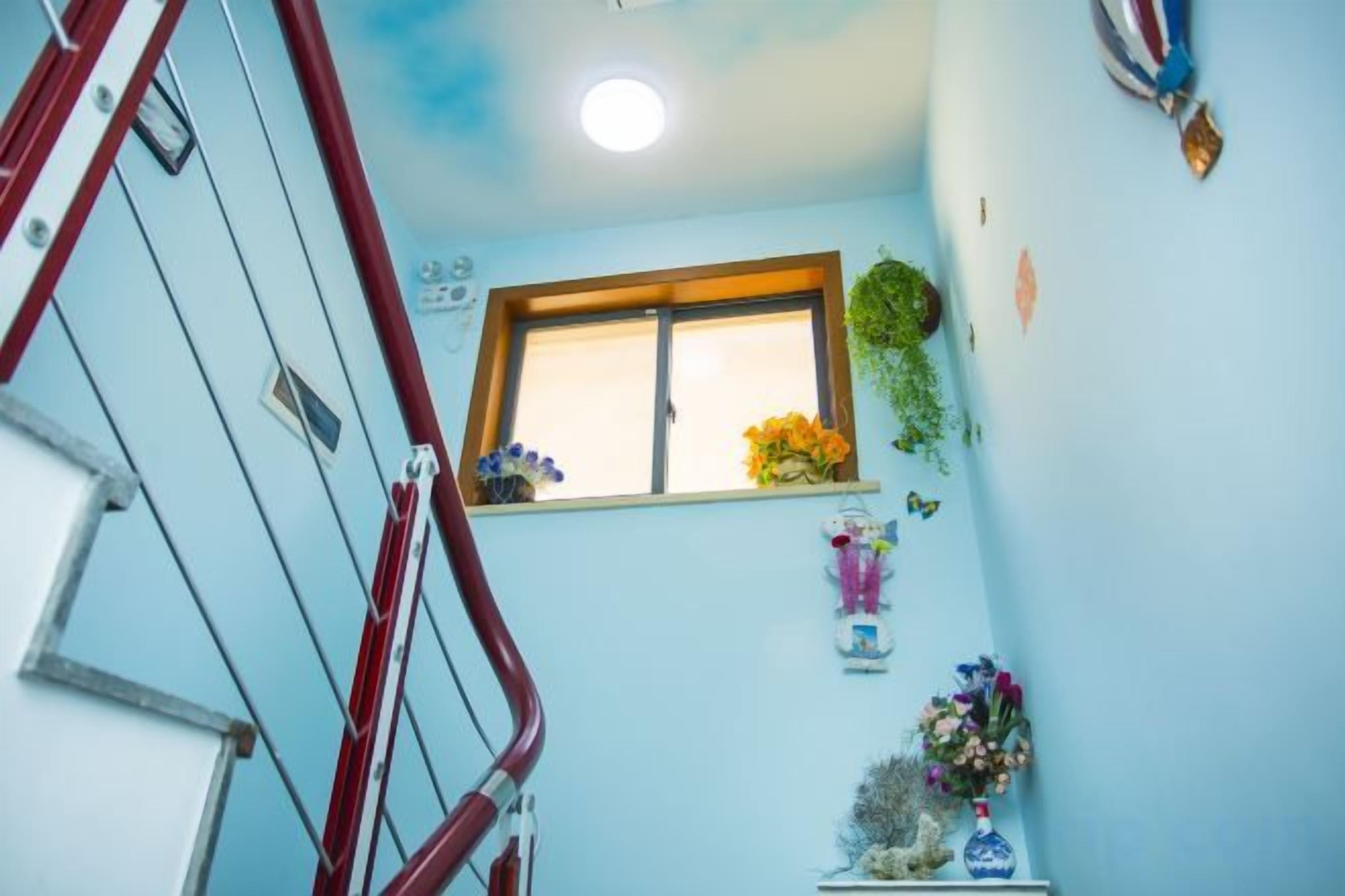A staircase with a red handrail, a window with a wooden frame, and a wall decorated with flowers and wall art.