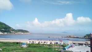 A coastal view with a beach, a row of buildings, and a mountainous backdrop. - Caiyuan Bihai Yuntian Hotel (Shengsi)