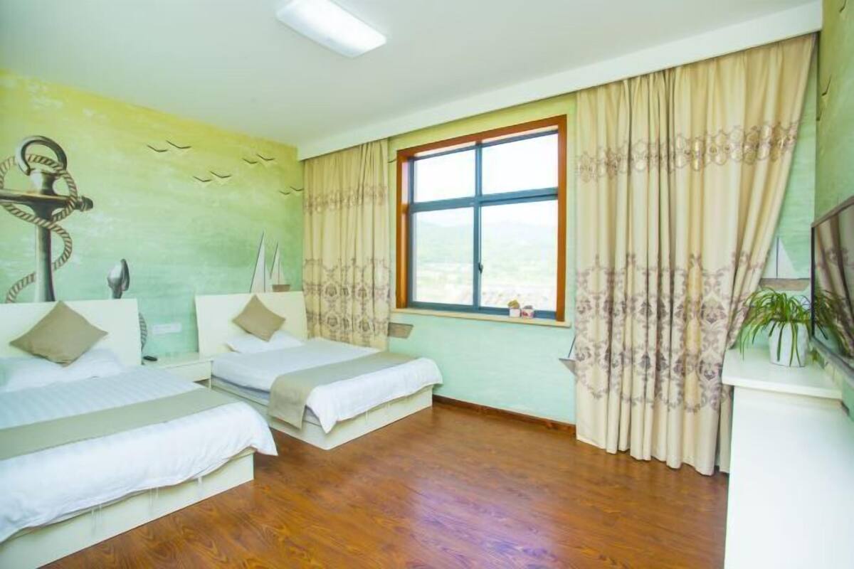 A hotel room with two beds, a large window with curtains, a wall-mounted TV, and a plant on a side table.