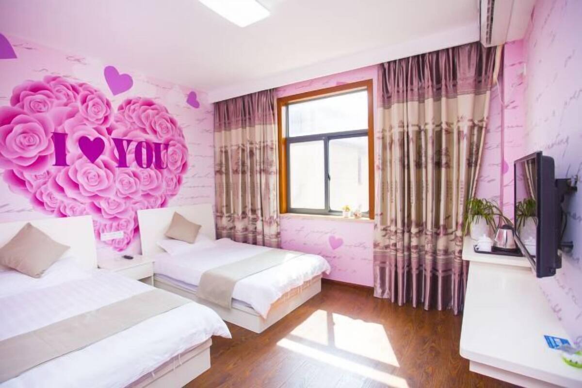 A hotel room with two beds, a large window, and a wall with a heart-shaped floral design.