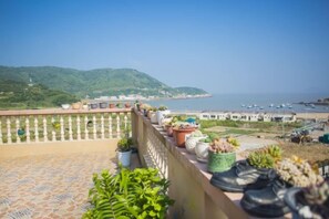 A terrace with potted plants and a view of the sea and boats. - Caiyuan Bihai Yuntian Hotel (Shengsi)
